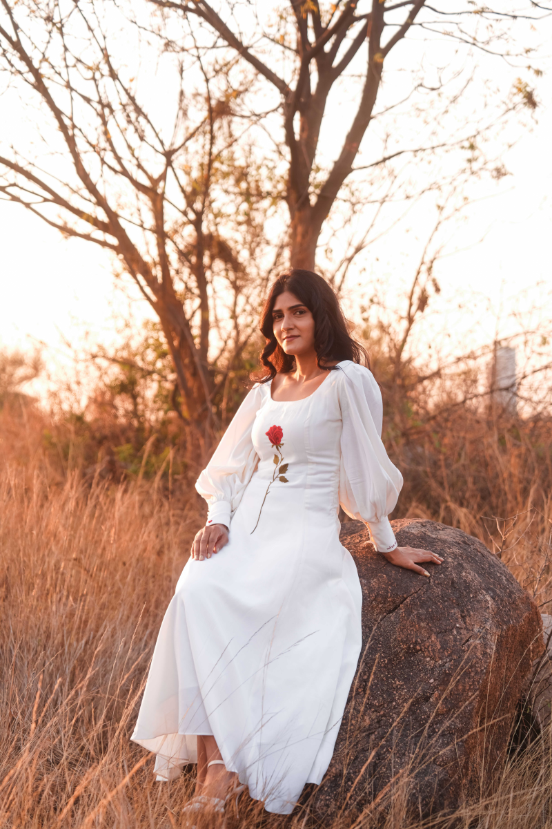 Woman in a white dress sitting on a rock in a field with trees in the background