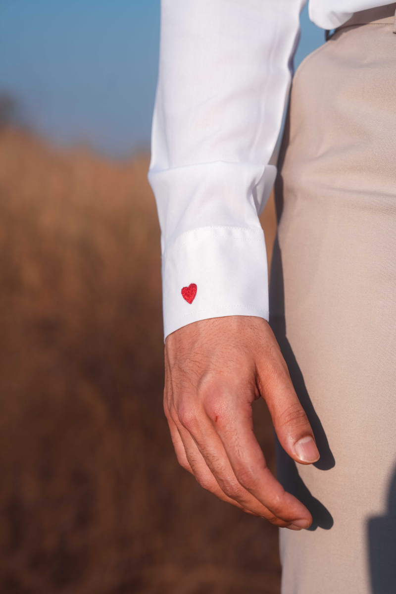 Hand wearing a white shirt with a red heart on the sleeve against a blurred natural background