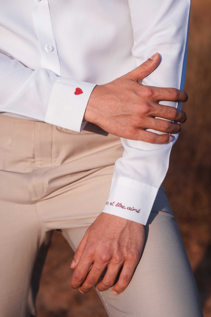 Close-up of a person wearing a white shirt with red text on the sleeve, paired with beige pants.