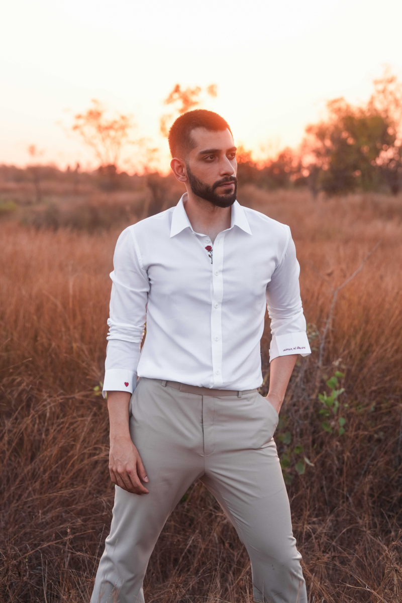 Man in a white shirt and beige pants standing in a field with sunset in the background