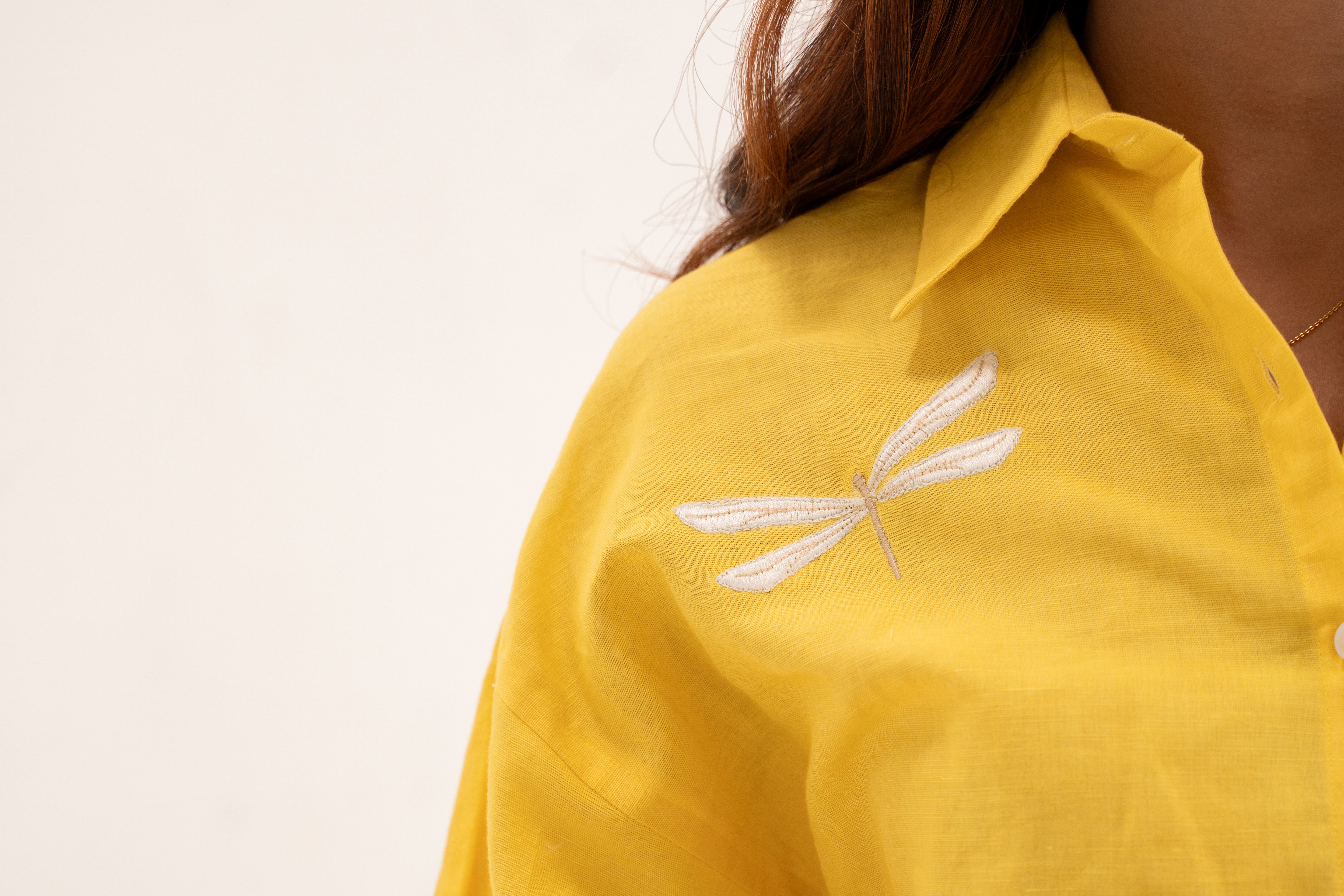 Yellow shirt with dragonfly embroidery on a plain background