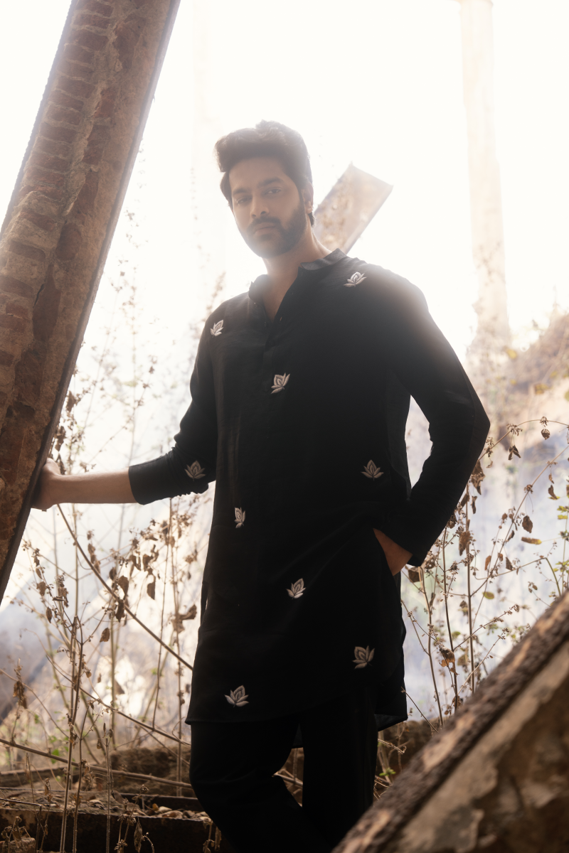 Man in a black coat standing among wooden planks and dry grass