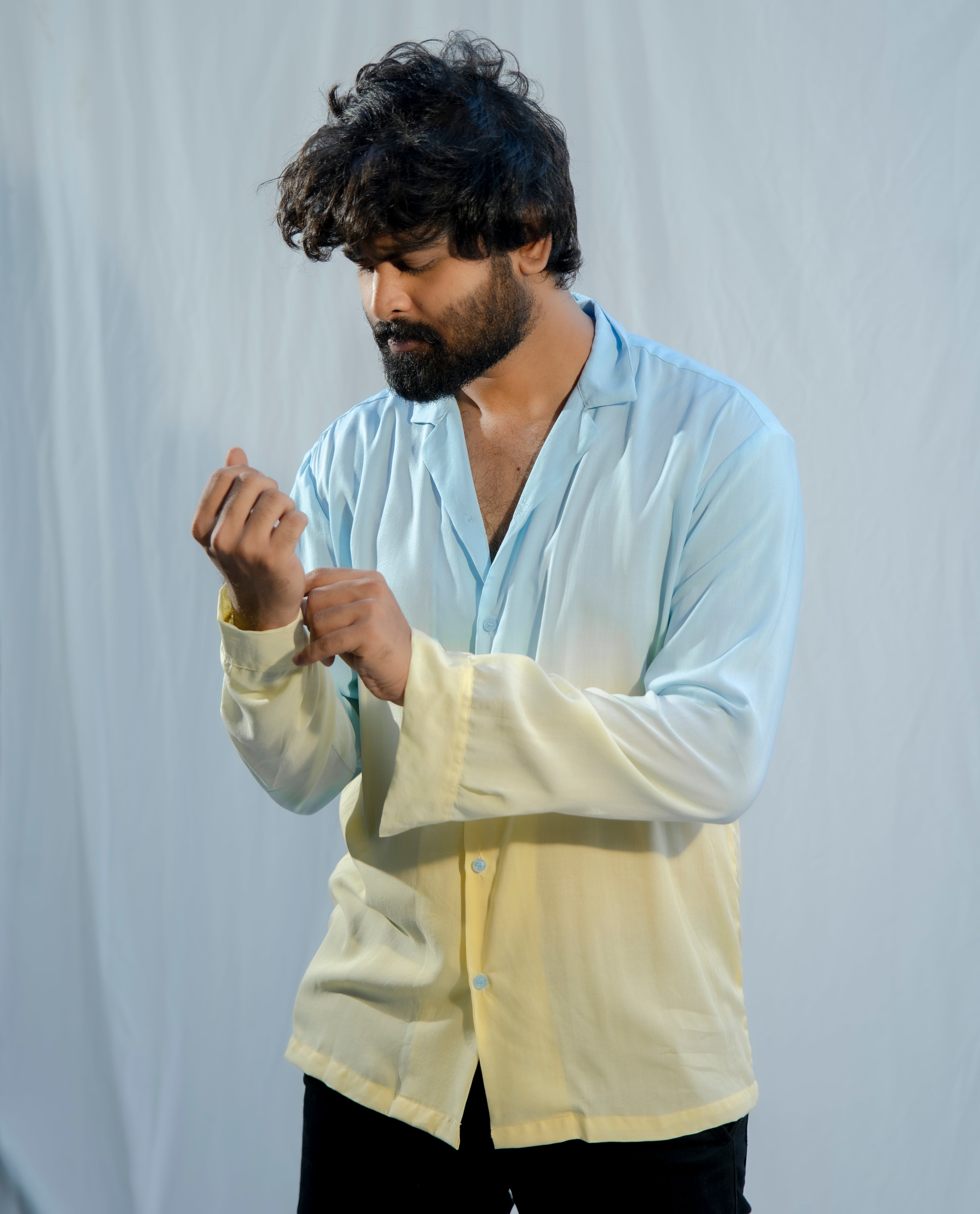 Man wearing a light blue shirt over a yellow shirt against a plain background