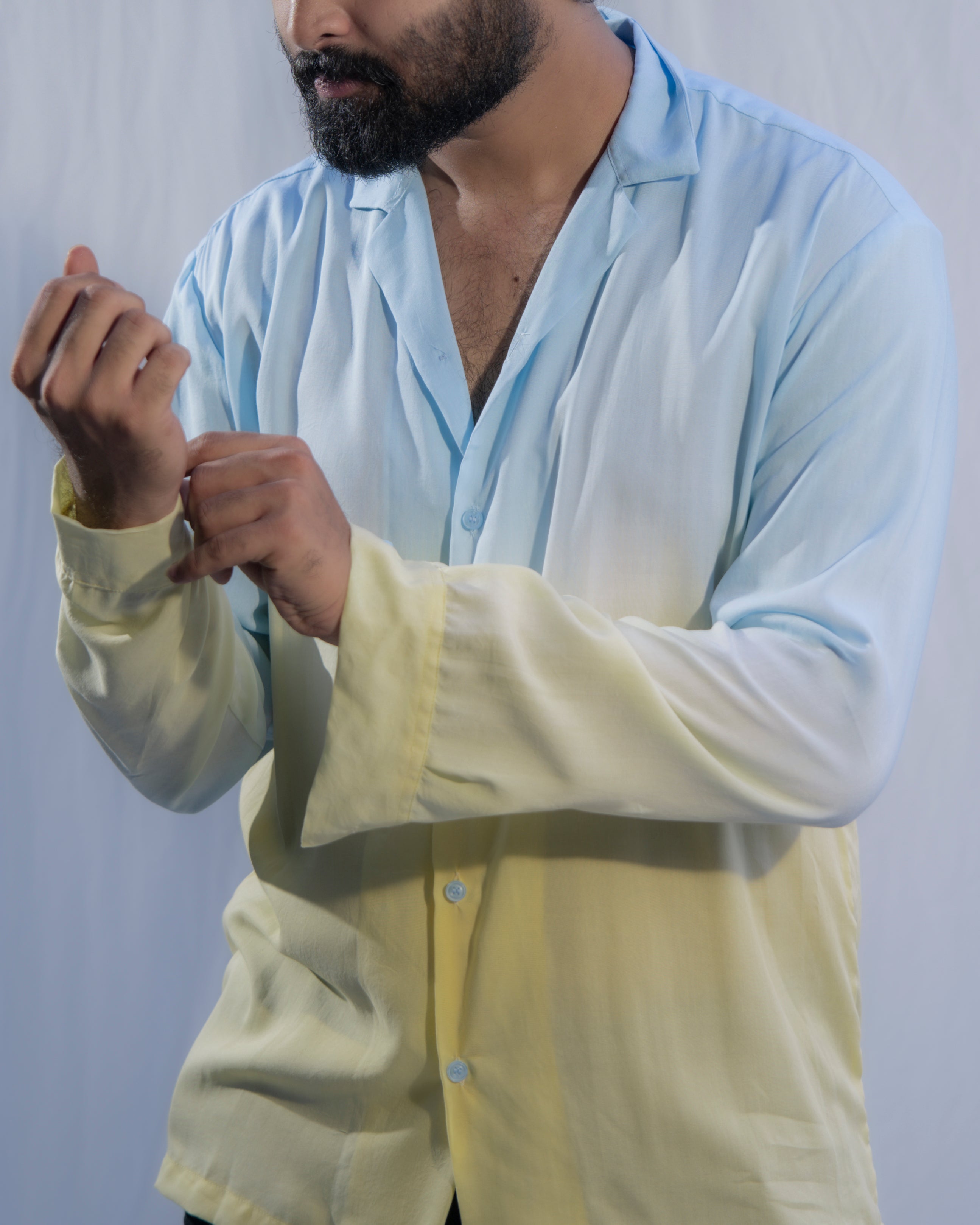 Person wearing a light blue shirt over a yellow vest against a plain background